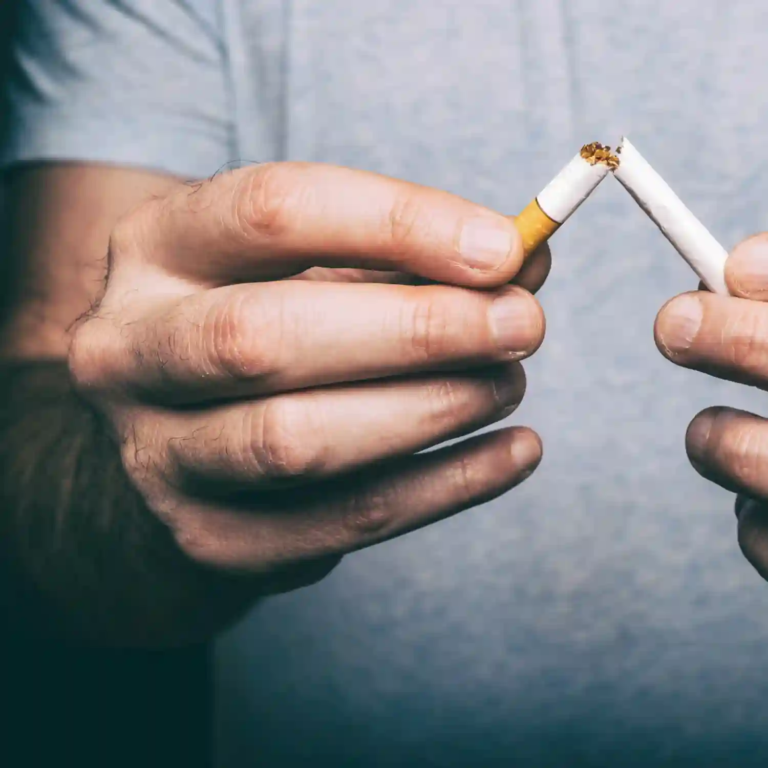 A close-up of two hands breaking a cigarette in half, with tobacco spilling out, against a clean white background — symbolizing a decisive act of quitting smoking and rejecting tobacco addiction.