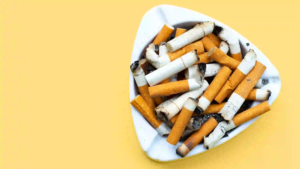 White triangular ashtray filled with burnt cigarette butts on a bright yellow background.