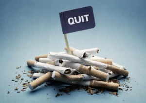 Pile of snapped cigarettes with a small flag labeled 'QUIT' emerging from the center against a blue background