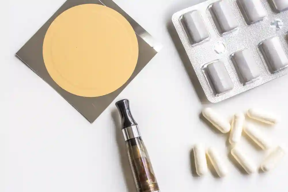 Nicotine patch, gum blister pack, capsules, and a vape pen arranged on a neutral surface as aids for smoking cessation